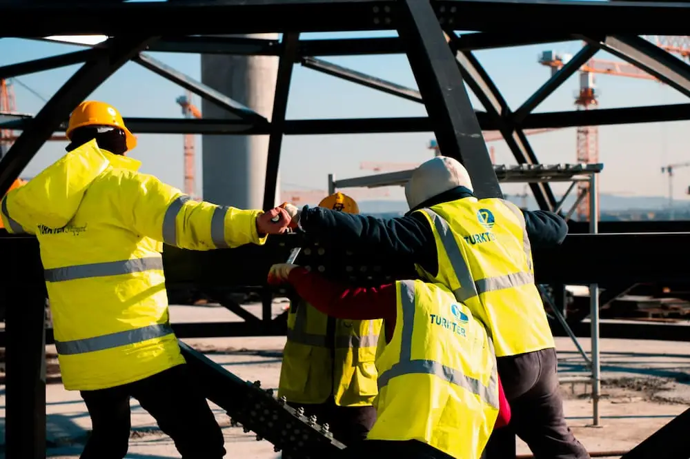 3 construction workers in high vis jackets on some metal structure. This demostrates health and safety in the workplace